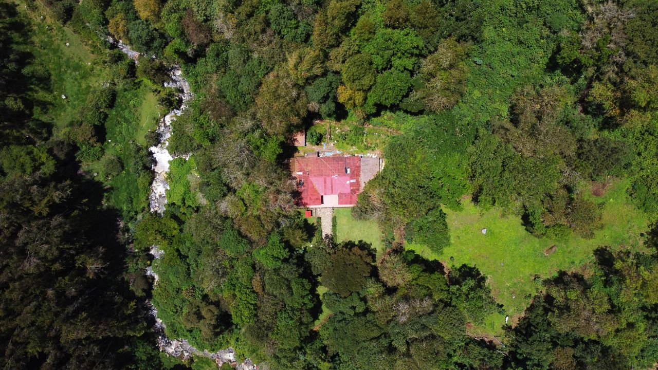 Drone view of a secluded house amidst dense green forest in Chocontá, Colombia near a flowing river.
