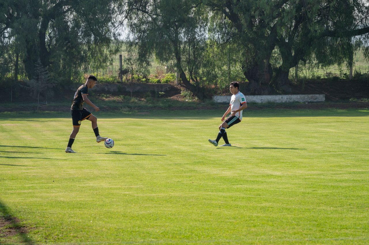 Two men playing a soccer match on a sunny outdoor field.
